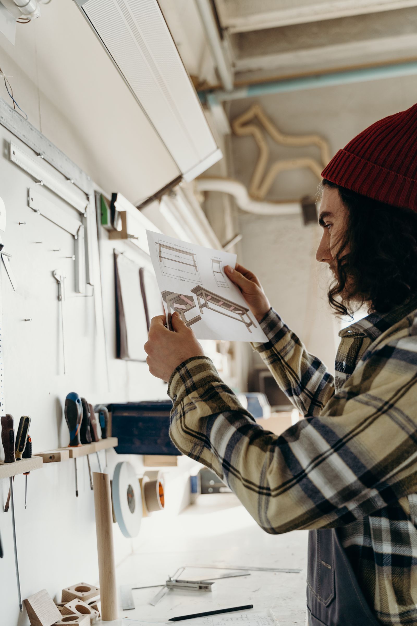 A maker in a workshop studying a technical drawing pinned to the wall