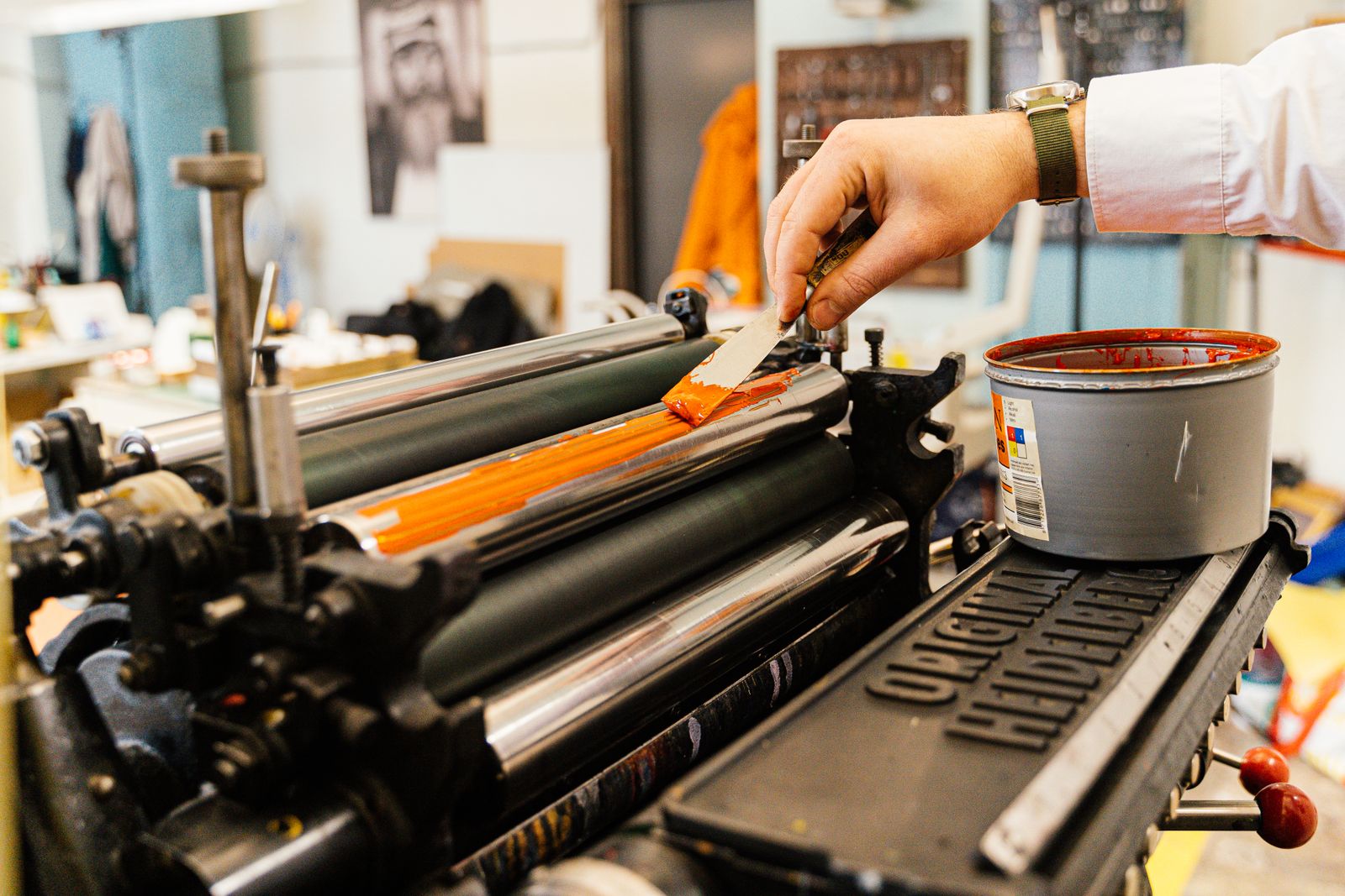 A hand rolling orange ink across the roller of a printing press