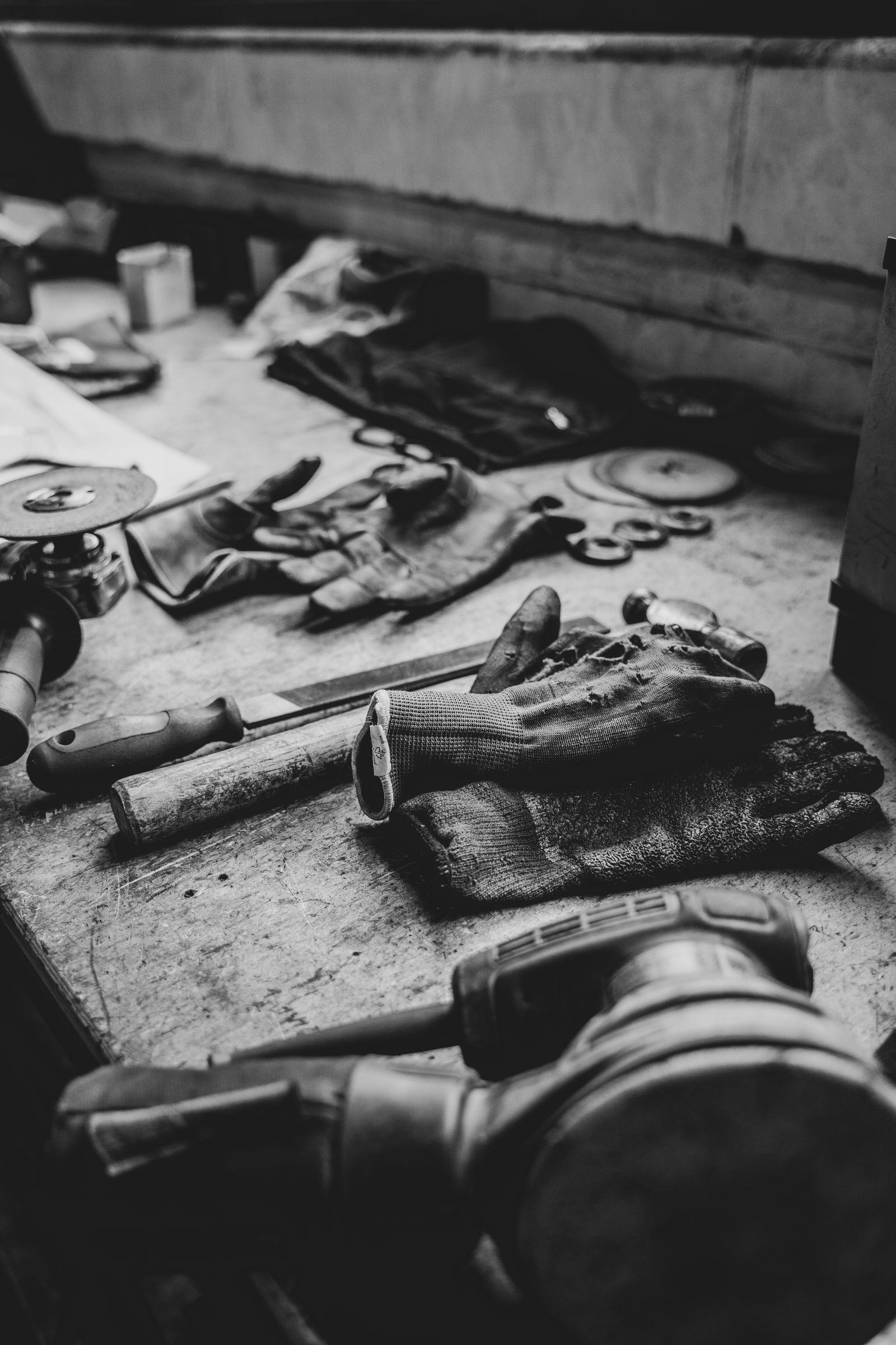Hand tools and work gloves laid out on a workshop bench, in black and white