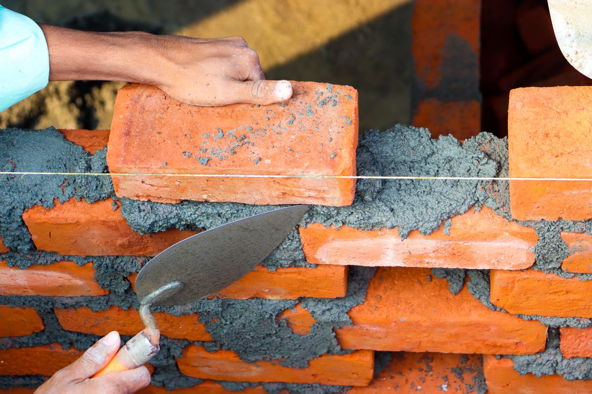 A bricklayer bedding a brick into mortar with a trowel