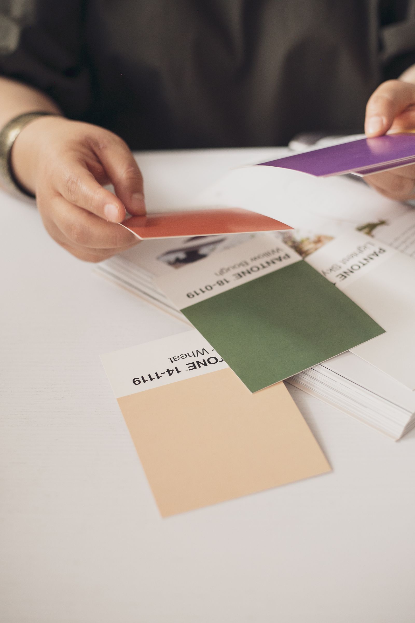 Hands comparing printed colour swatches on a studio desk